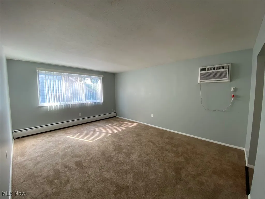 Carpeted spare room featuring a baseboard radiator and a wall mounted air conditioner