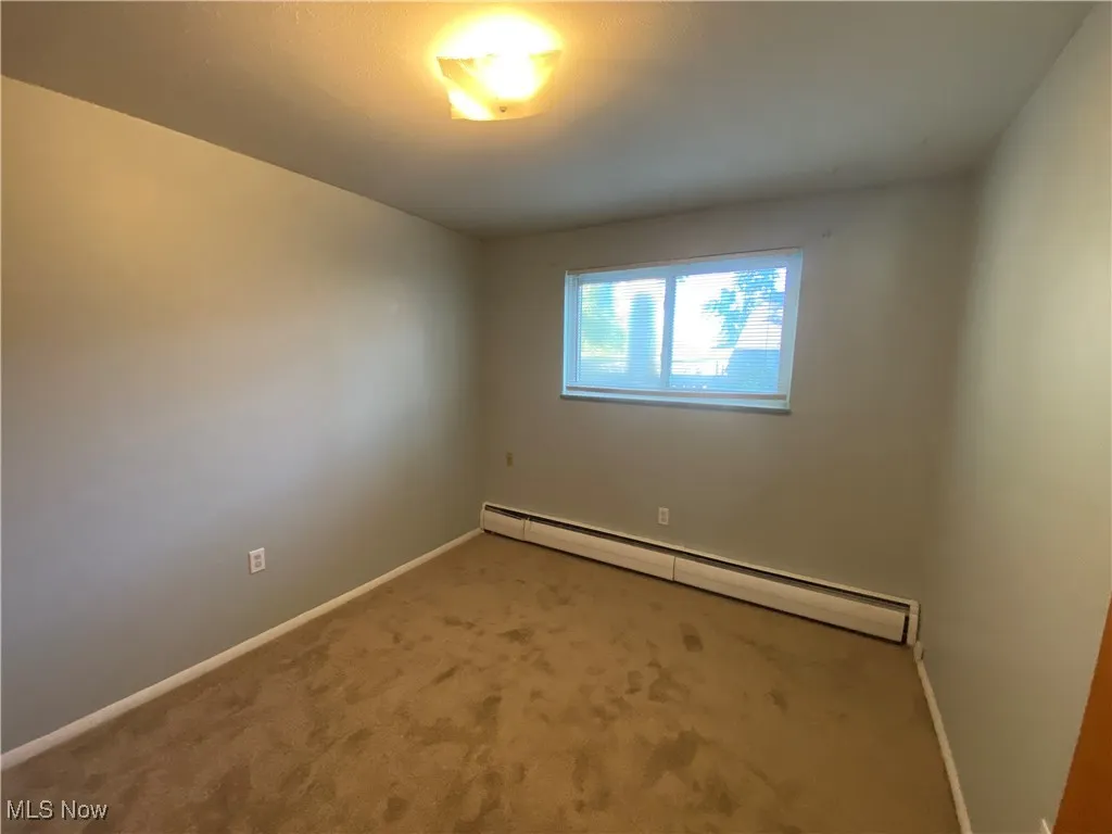 Spare room with a baseboard heating unit and carpet