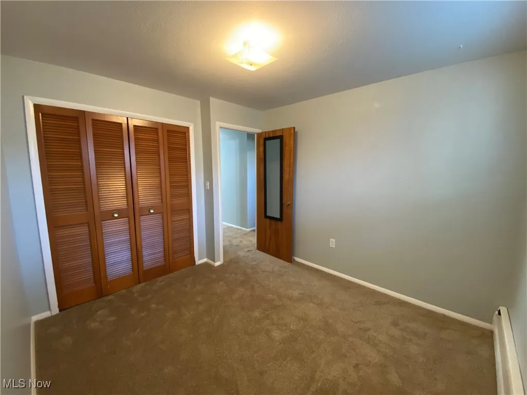 Unfurnished bedroom featuring a baseboard heating unit, carpet, and a closet