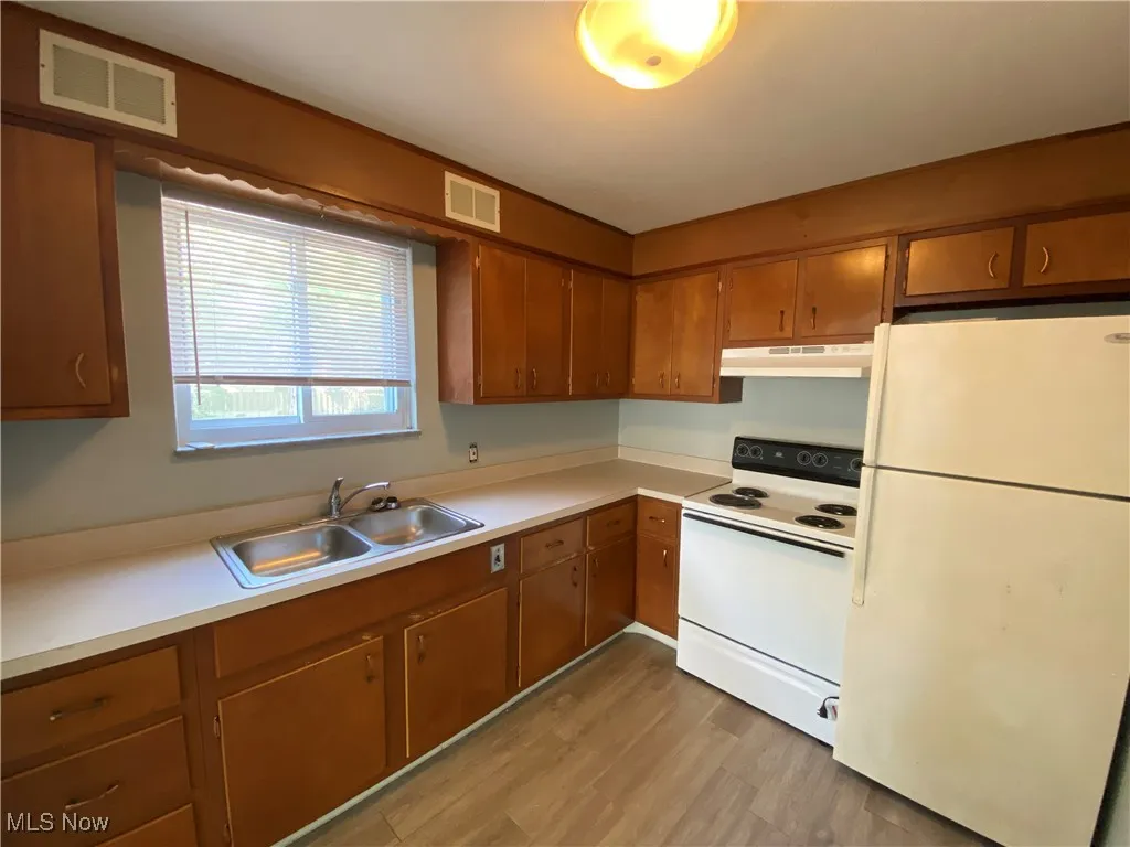 Kitchen with white appliances, light countertops, light wood-style floors, brown cabinets, and under cabinet range hood