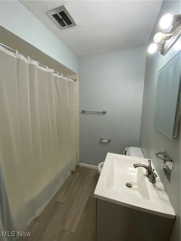 Full bath with wood finished floors, vanity, and shower / bath combo with shower curtain