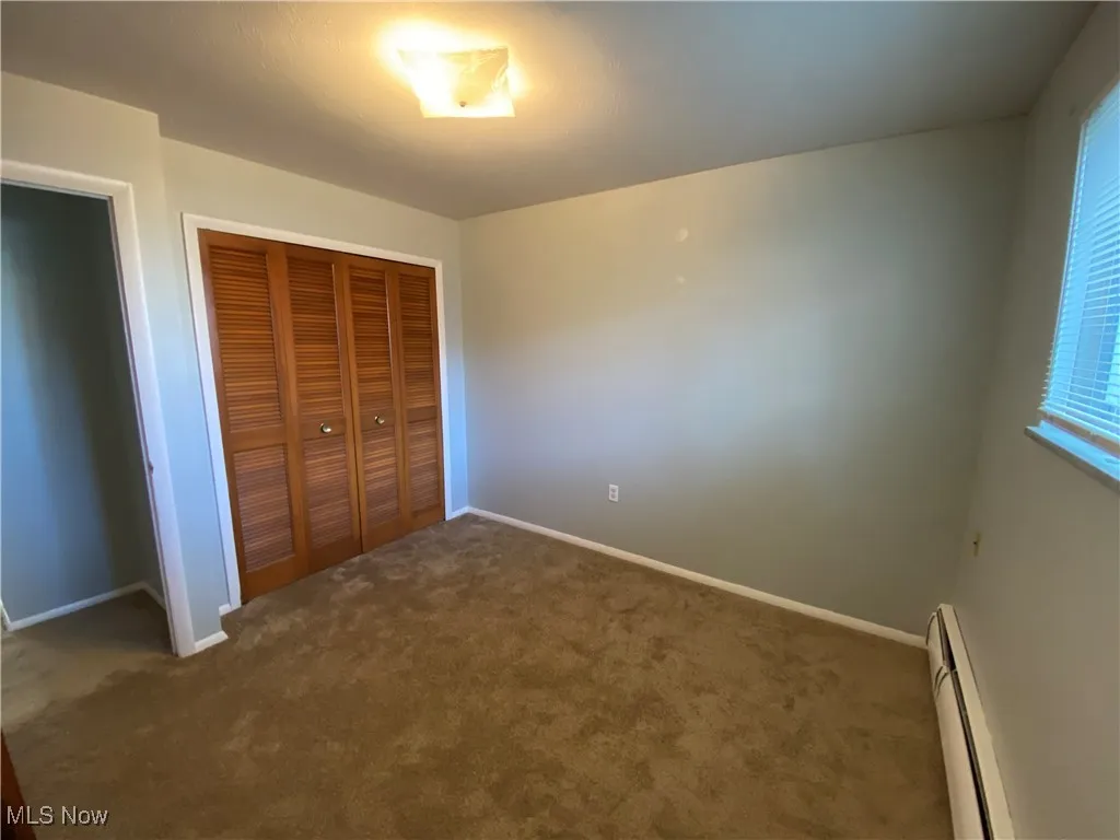Unfurnished bedroom featuring baseboard heating, carpet, and a closet