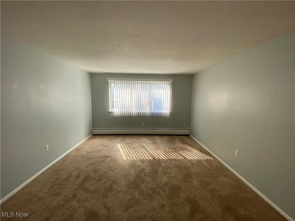 Carpeted empty room featuring baseboard heating and a textured ceiling