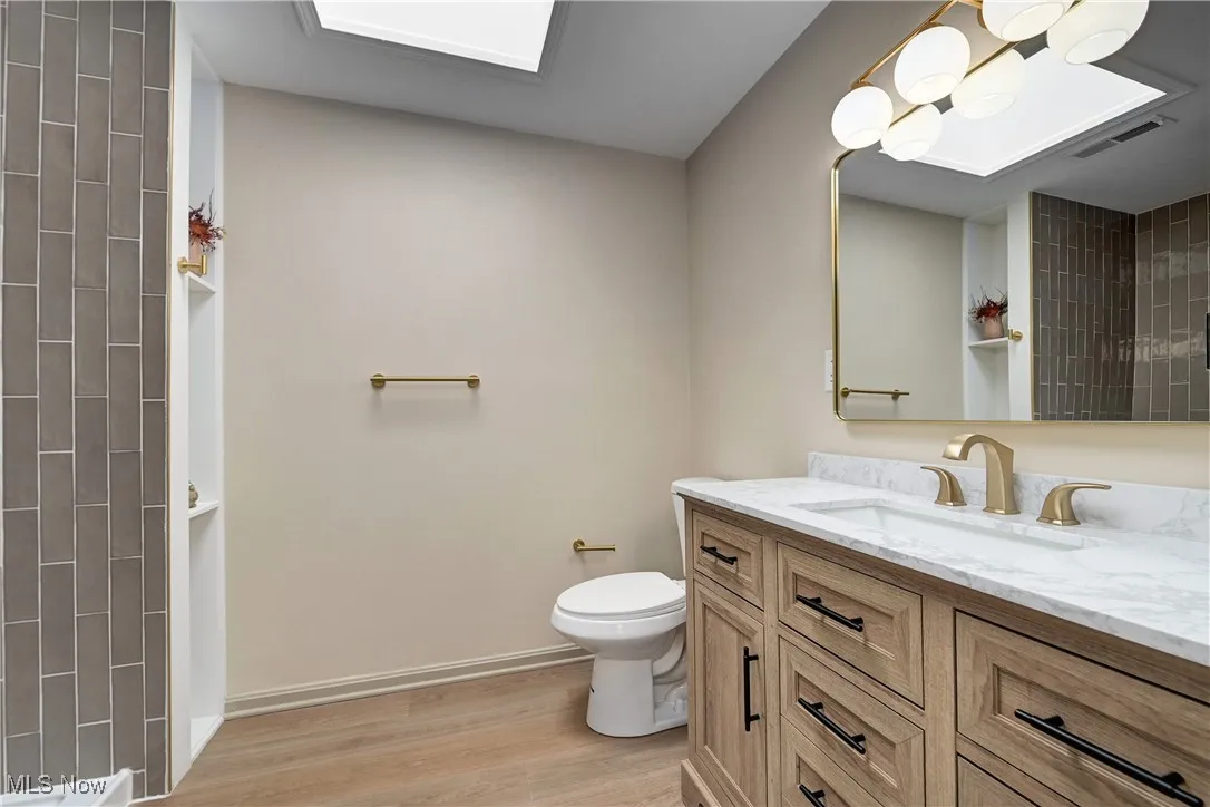 Bathroom featuring vanity, wood finished floors, a tile shower, and a skylight