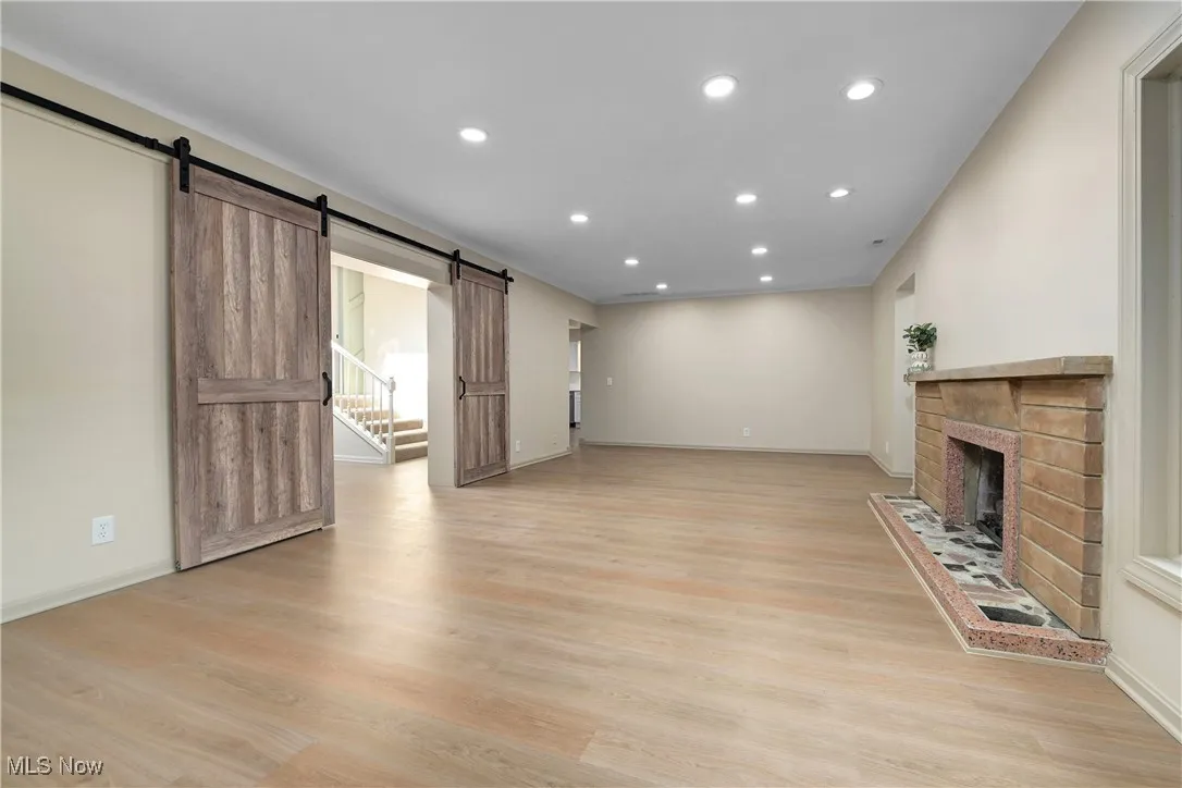 Unfurnished living room with a barn door, recessed lighting, light wood-style floors, a fireplace, and stairs