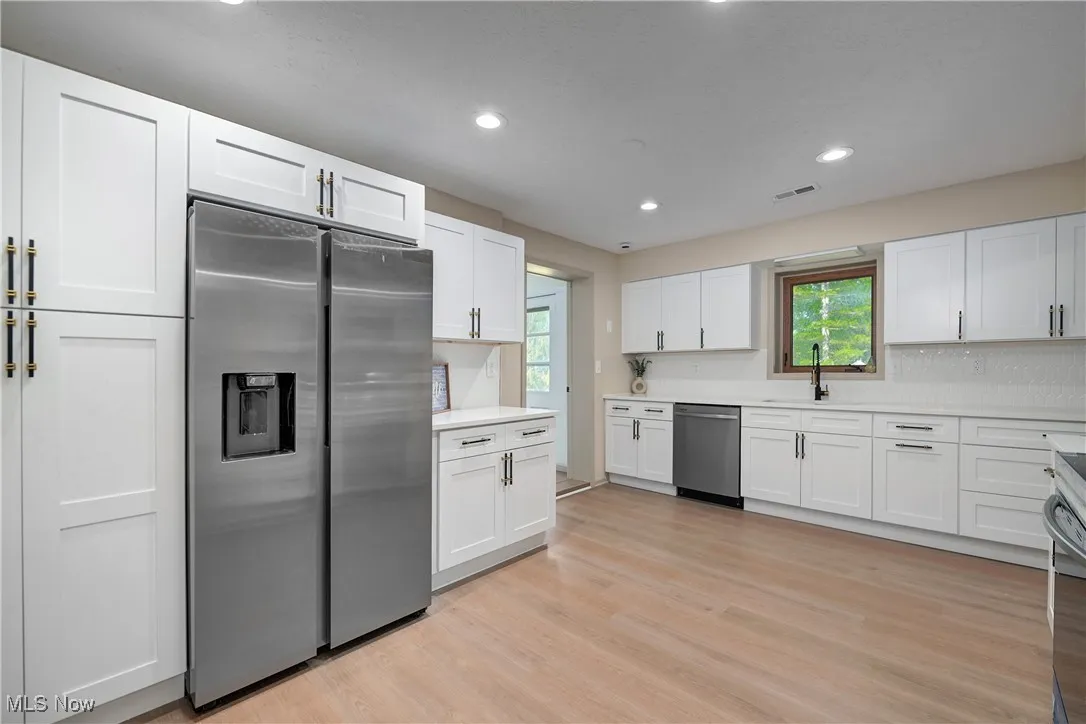 Kitchen with appliances with stainless steel finishes, healthy amount of natural light, light wood-type flooring, recessed lighting, and white cabinets