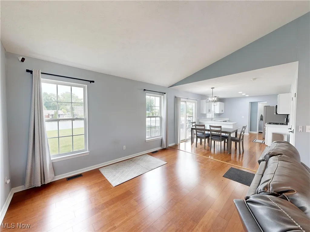 Living area featuring light wood-style floors, vaulted ceiling, plenty of natural light, and a chandelier