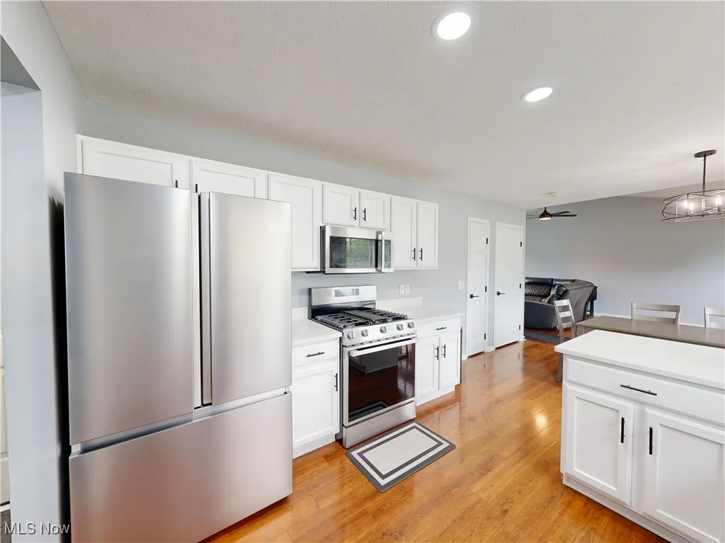 Kitchen featuring appliances with stainless steel finishes, light wood-style flooring, white cabinets, light countertops, and a ceiling fan