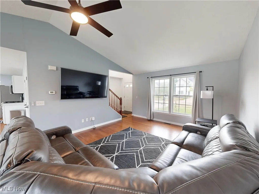 Living area featuring wood finished floors, stairway, ceiling fan, and lofted ceiling