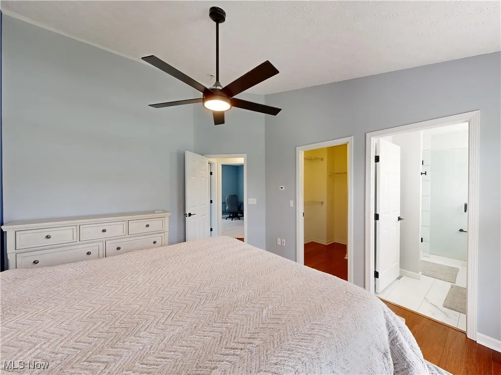 Bedroom featuring wood finished floors, a spacious closet, ceiling fan, and ensuite bathroom
