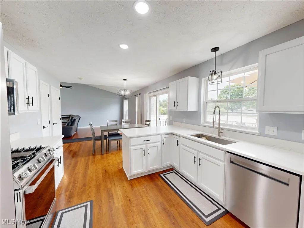 Kitchen featuring stainless steel appliances, white cabinets, light countertops, a textured ceiling, and decorative light fixtures