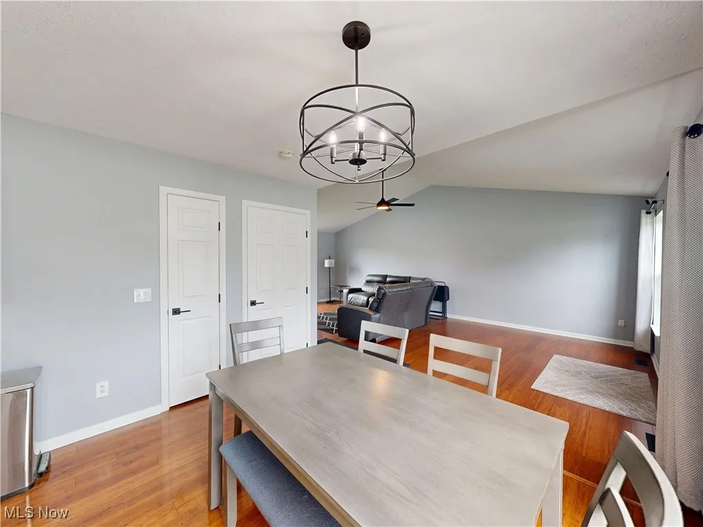 Dining space featuring wood finished floors, a chandelier, vaulted ceiling, and ceiling fan