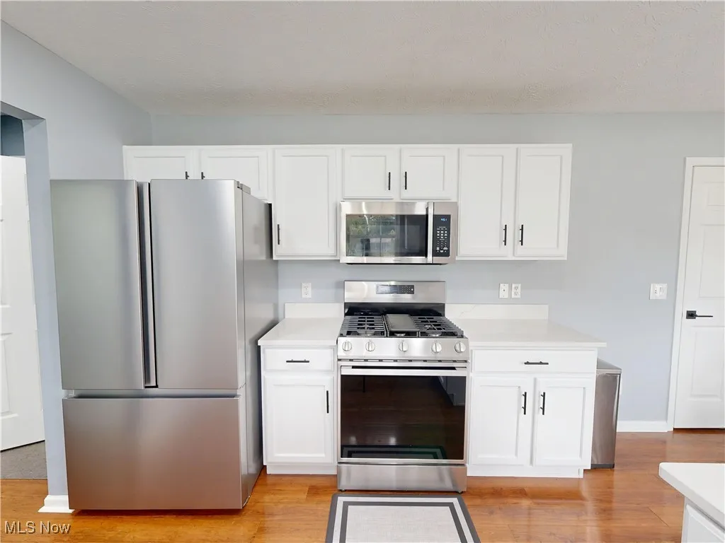 Kitchen featuring stainless steel appliances, light countertops, light wood finished floors, and white cabinetry