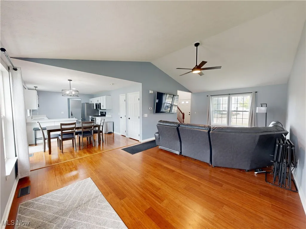 Living area with lofted ceiling, light wood-style floors, stairs, and a ceiling fan