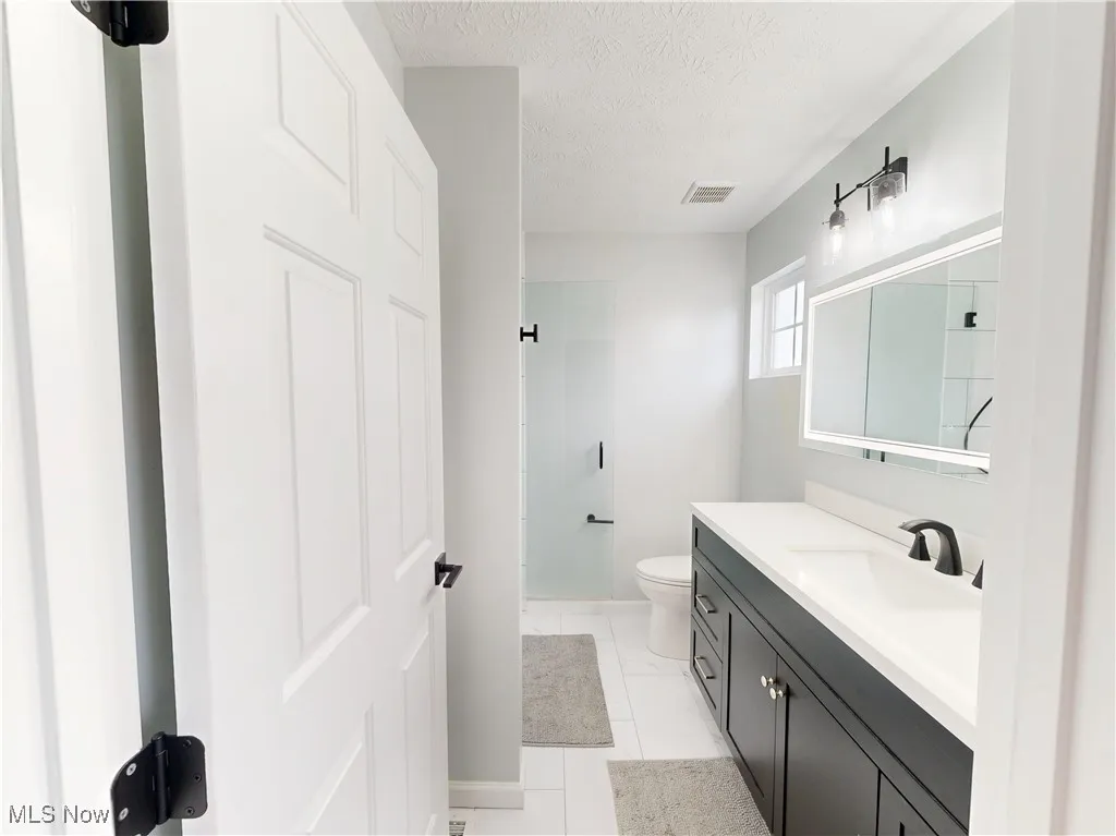 Full bath featuring a textured ceiling, vanity, a shower, and tile patterned floors