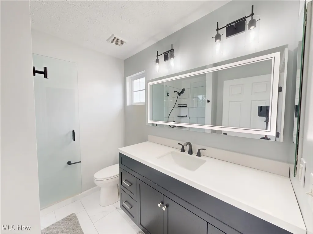 Bathroom with a textured ceiling, vanity, and a tile shower