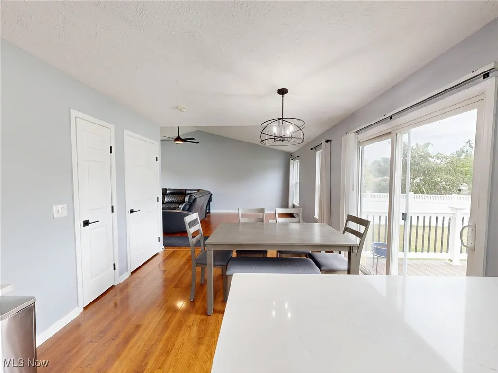 Dining area featuring light wood-style flooring, a textured ceiling, vaulted ceiling, a ceiling fan, and a chandelier