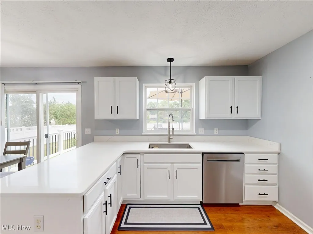 Kitchen with stainless steel dishwasher, light wood-style floors, white cabinets, light countertops, and a textured ceiling