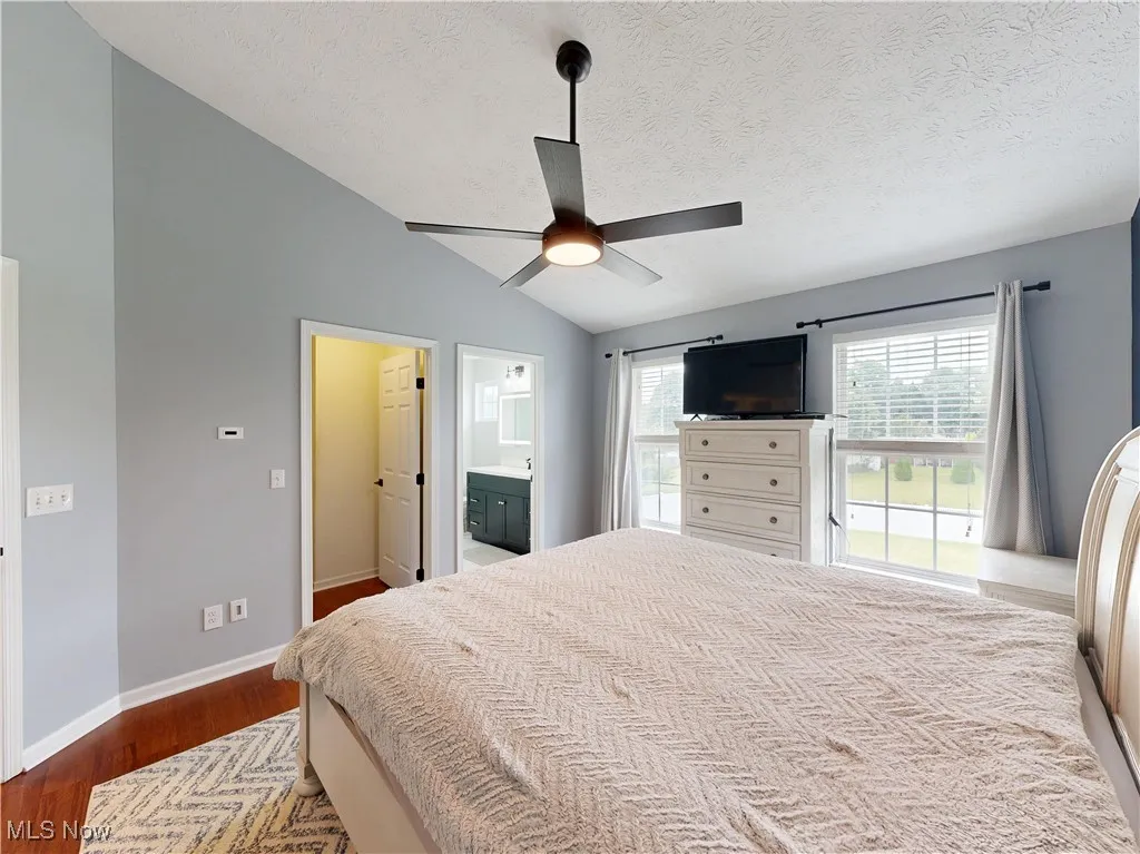 Bedroom with lofted ceiling, wood finished floors, a textured ceiling, ceiling fan, and ensuite bath