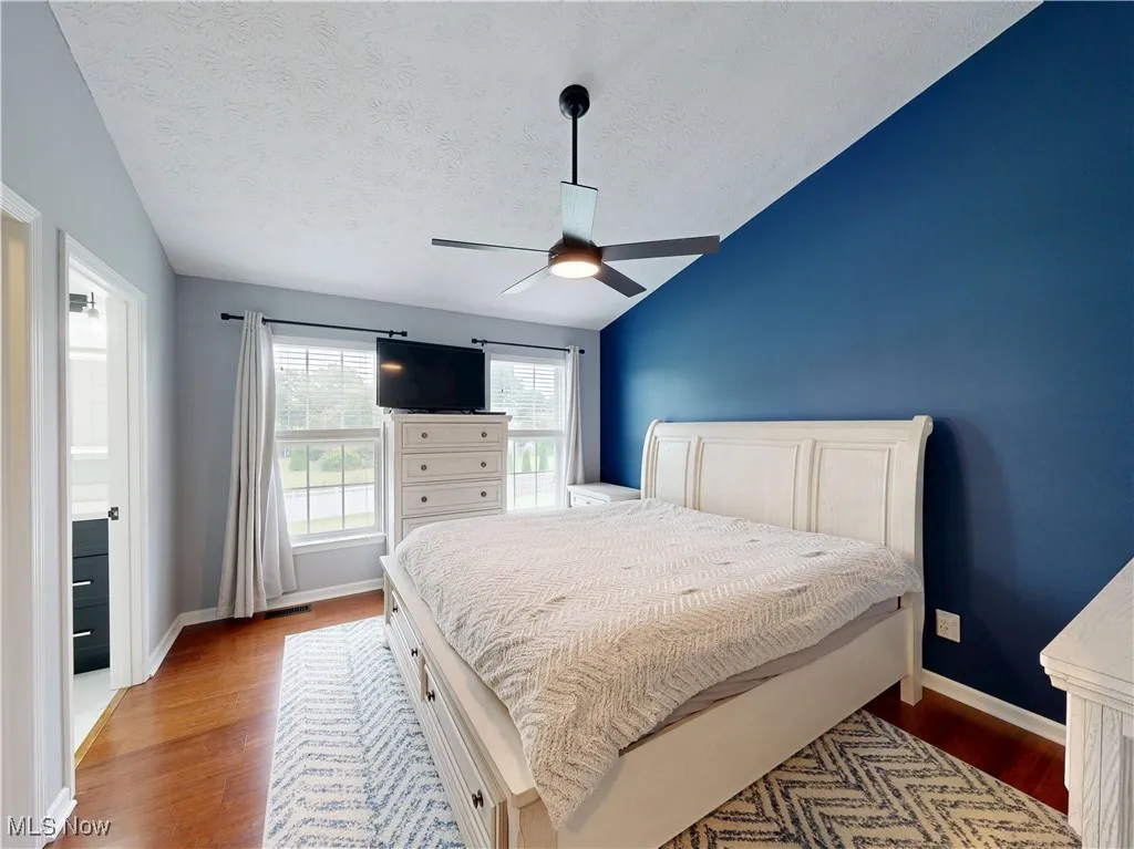 Bedroom featuring lofted ceiling, wood finished floors, a textured ceiling, and a ceiling fan