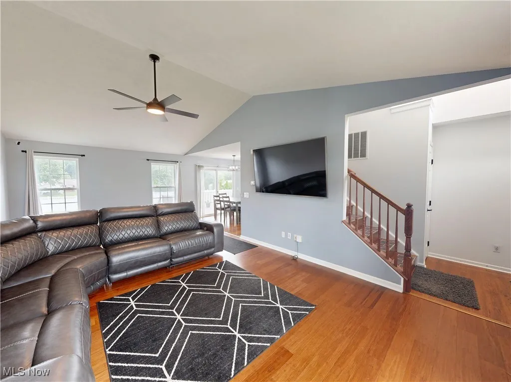 Living area featuring plenty of natural light, wood finished floors, lofted ceiling, stairs, and a ceiling fan