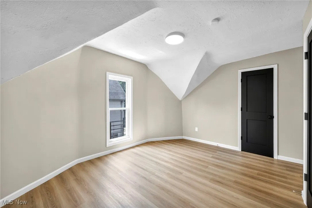 Bonus room featuring a textured ceiling, light wood-style flooring, and lofted ceiling