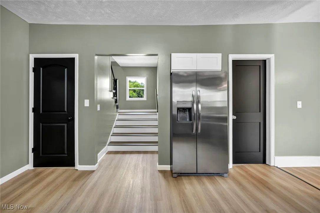 Kitchen with stainless steel fridge with ice dispenser, a textured ceiling, white cabinets, and light wood-style flooring