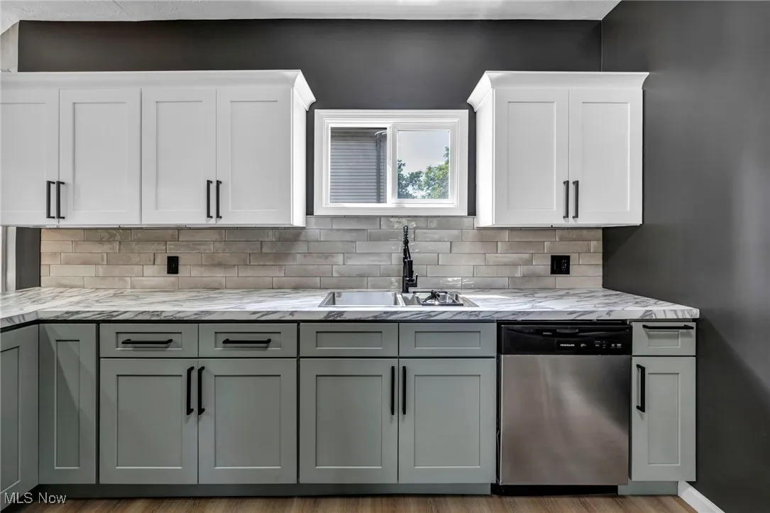 Kitchen with stainless steel dishwasher, light stone countertops, tasteful backsplash, and white cabinets