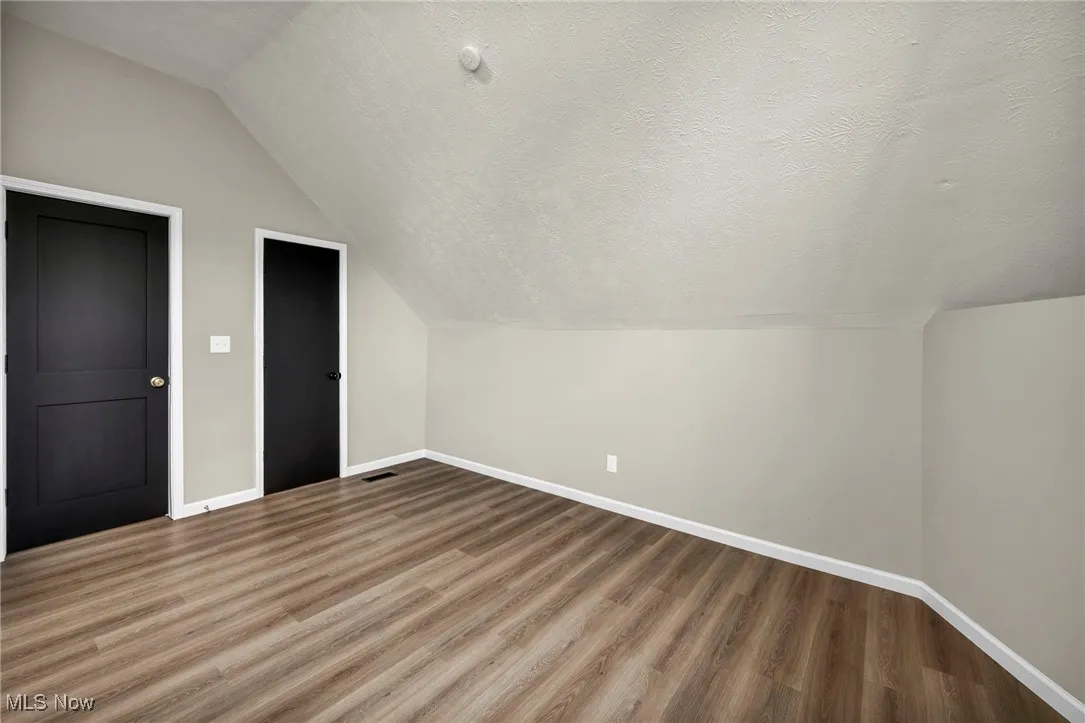 Additional living space with a textured ceiling, lofted ceiling, and wood finished floors