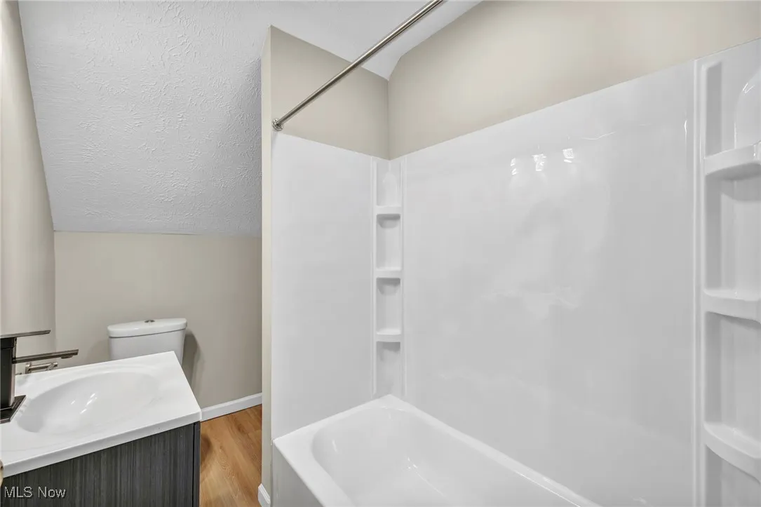 Full bath with lofted ceiling, shower / bathtub combination, wood finished floors, a textured ceiling, and vanity