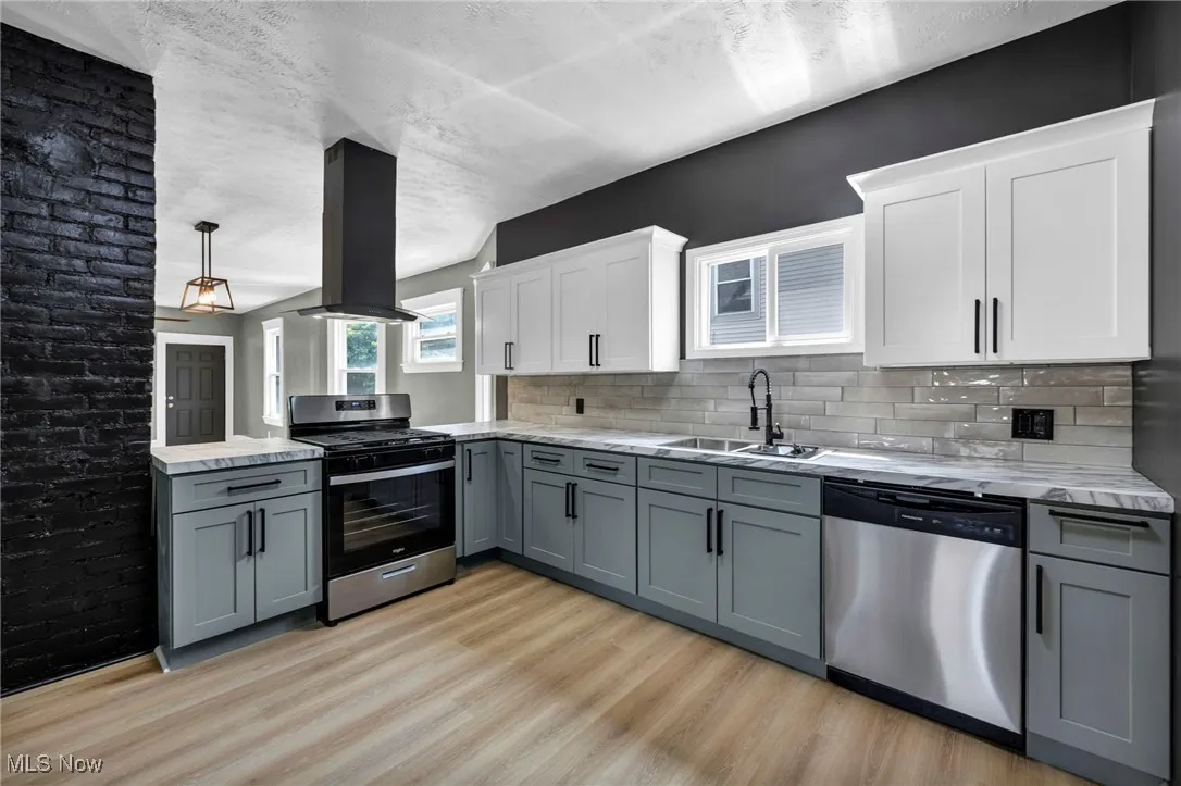 Kitchen with gray cabinets, appliances with stainless steel finishes, a textured ceiling, island range hood, and a peninsula