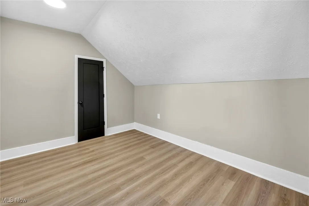 Bonus room with a textured ceiling, light wood-type flooring, and lofted ceiling