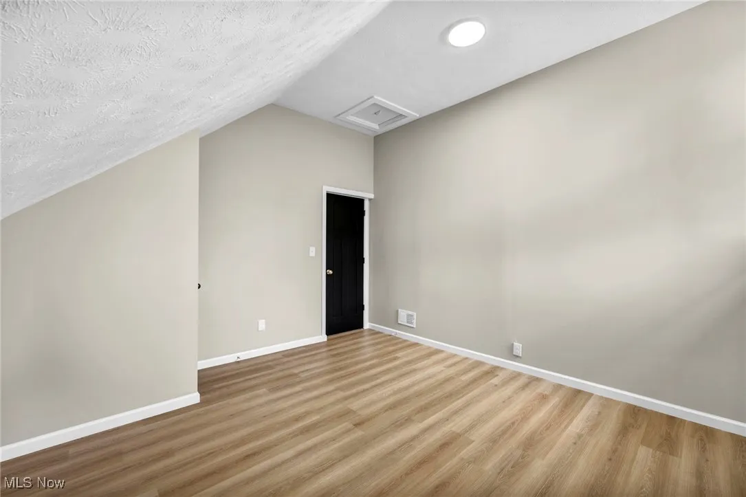 Additional living space with attic access, vaulted ceiling, a textured ceiling, and wood finished floors