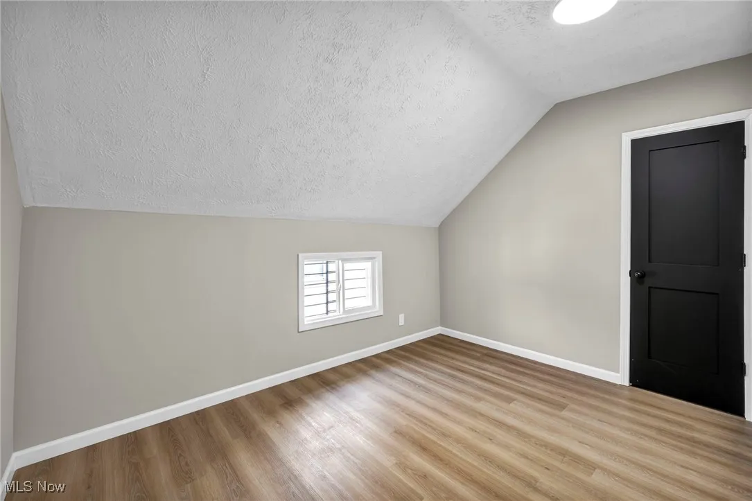 Additional living space featuring a textured ceiling, vaulted ceiling, and wood finished floors