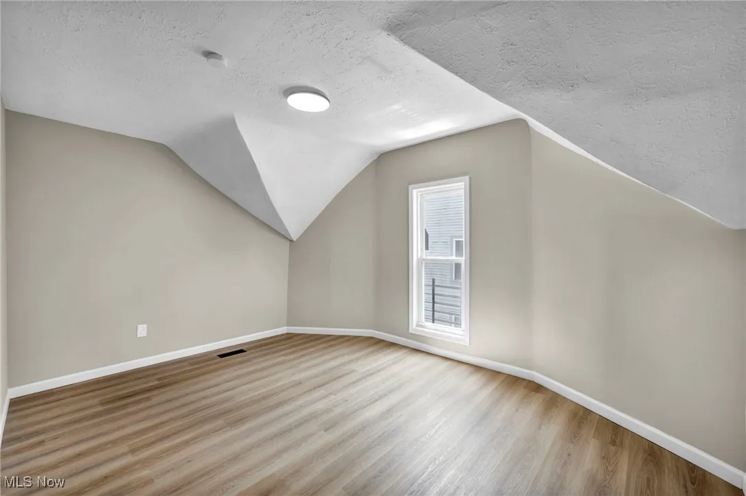 Additional living space with a textured ceiling, wood finished floors, and lofted ceiling