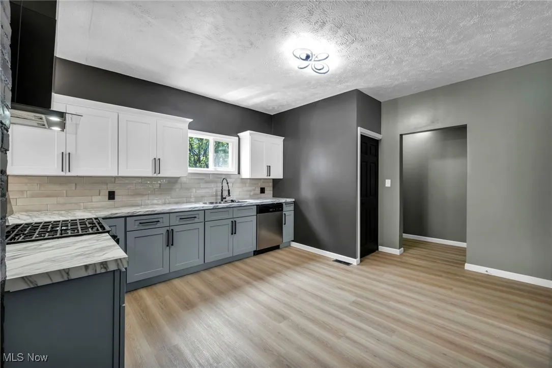 Kitchen with decorative backsplash, light wood-style flooring, a textured ceiling, white cabinetry, and dishwasher