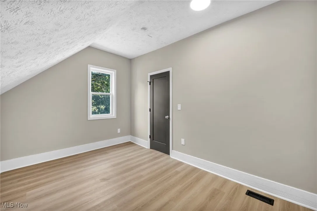Additional living space with a textured ceiling, light wood-style floors, and vaulted ceiling
