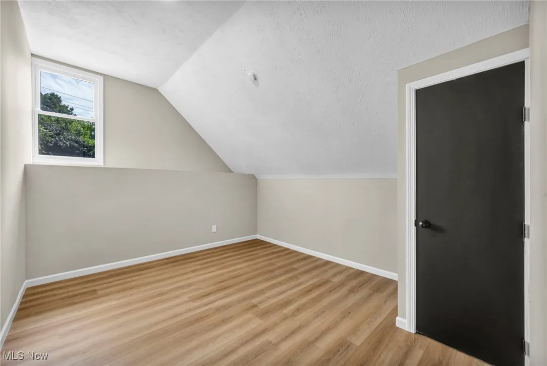 Bonus room featuring a textured ceiling, light wood-style floors, and vaulted ceiling