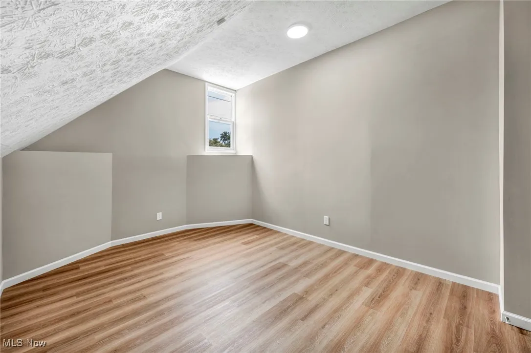Additional living space featuring a textured ceiling, light wood finished floors, and vaulted ceiling