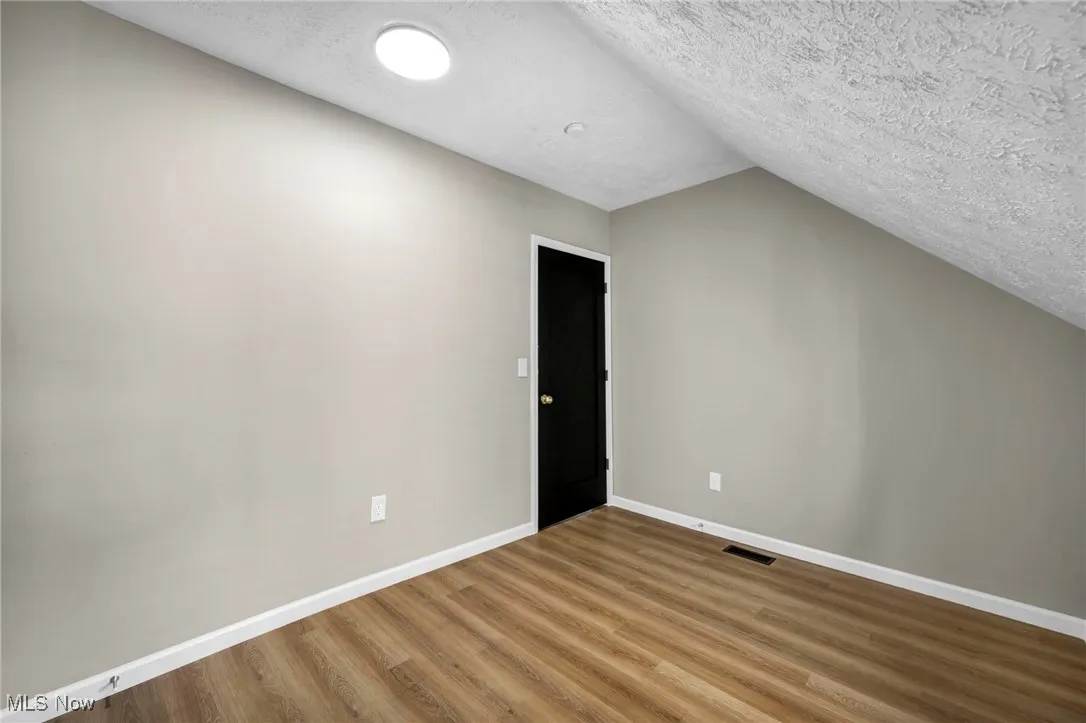 Additional living space with a textured ceiling, vaulted ceiling, and wood finished floors