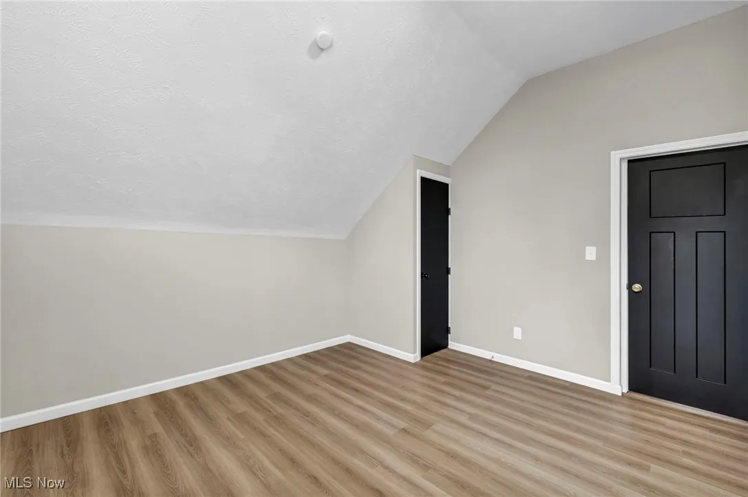 Additional living space featuring lofted ceiling, light wood-type flooring, and a textured ceiling