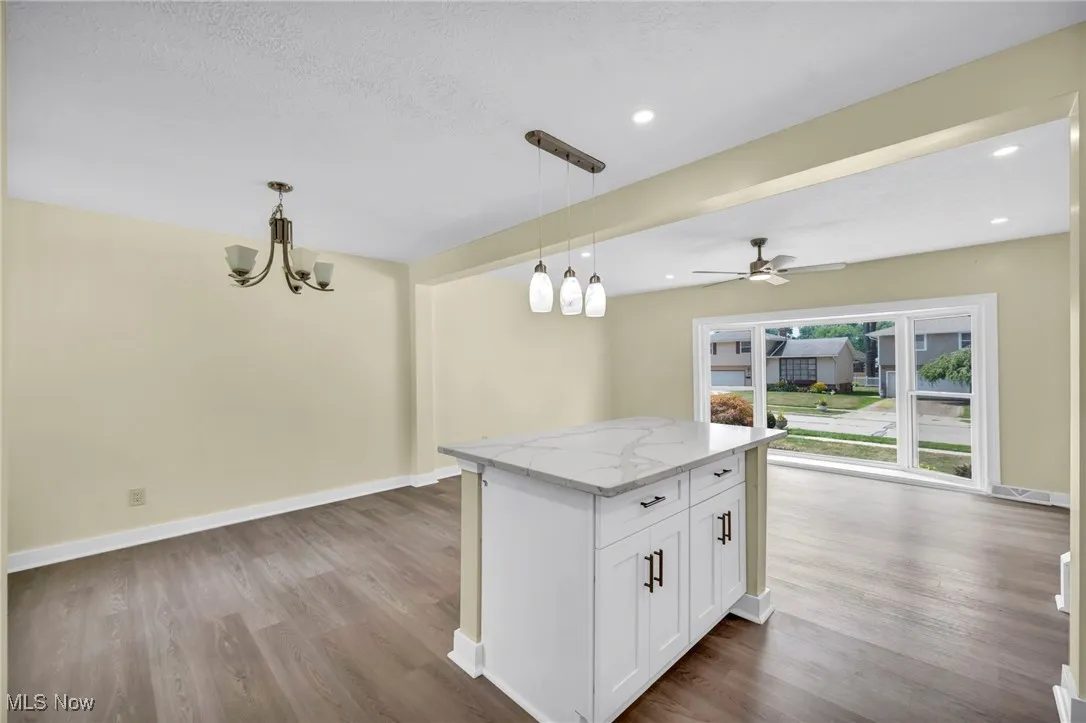 Kitchen with dark wood-type flooring, light stone countertops, white cabinetry, a kitchen island, and recessed lighting