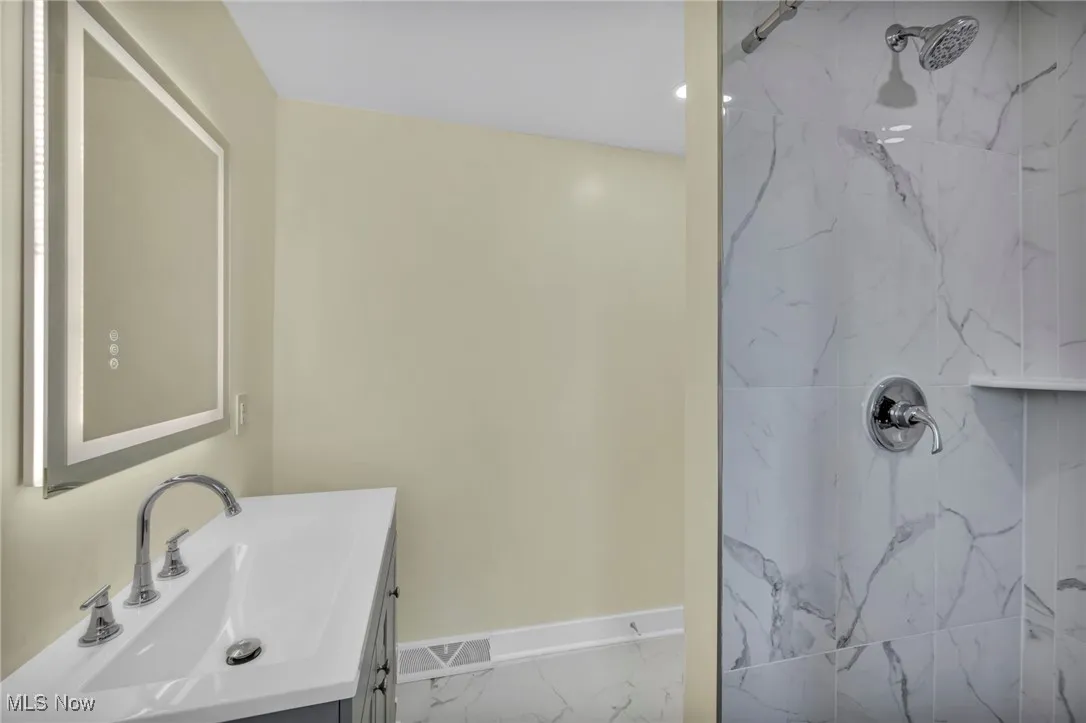 Full bathroom with a marble finish shower, vanity, and marble look tiles