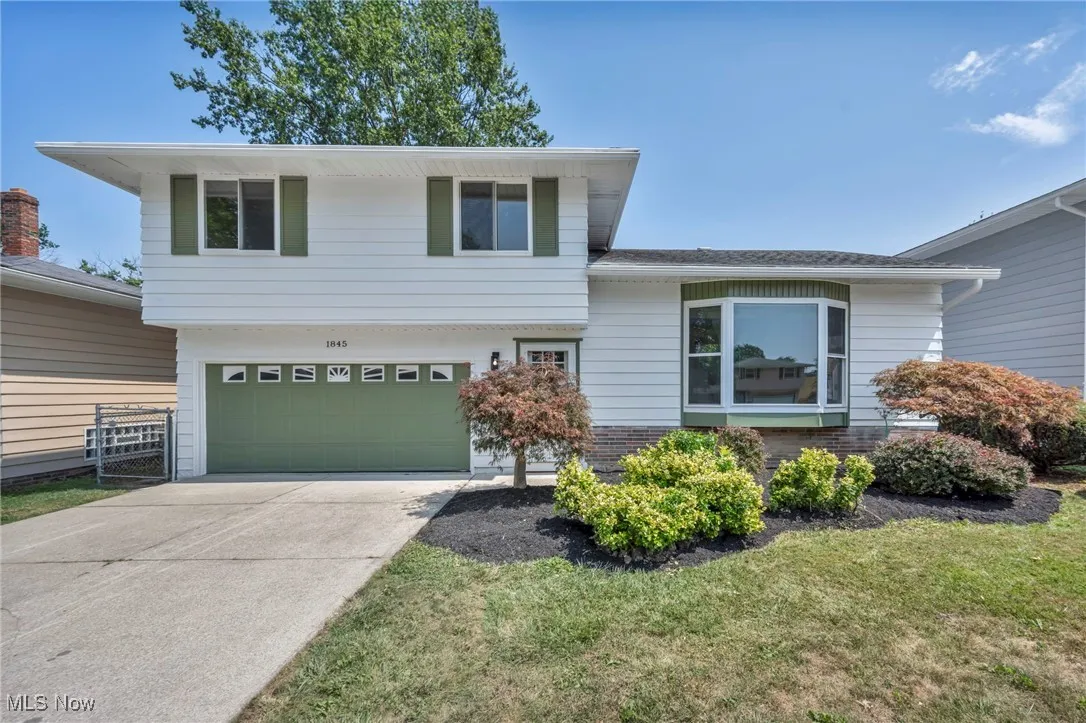 Tri-level home with a garage, driveway, brick siding, and a front yard