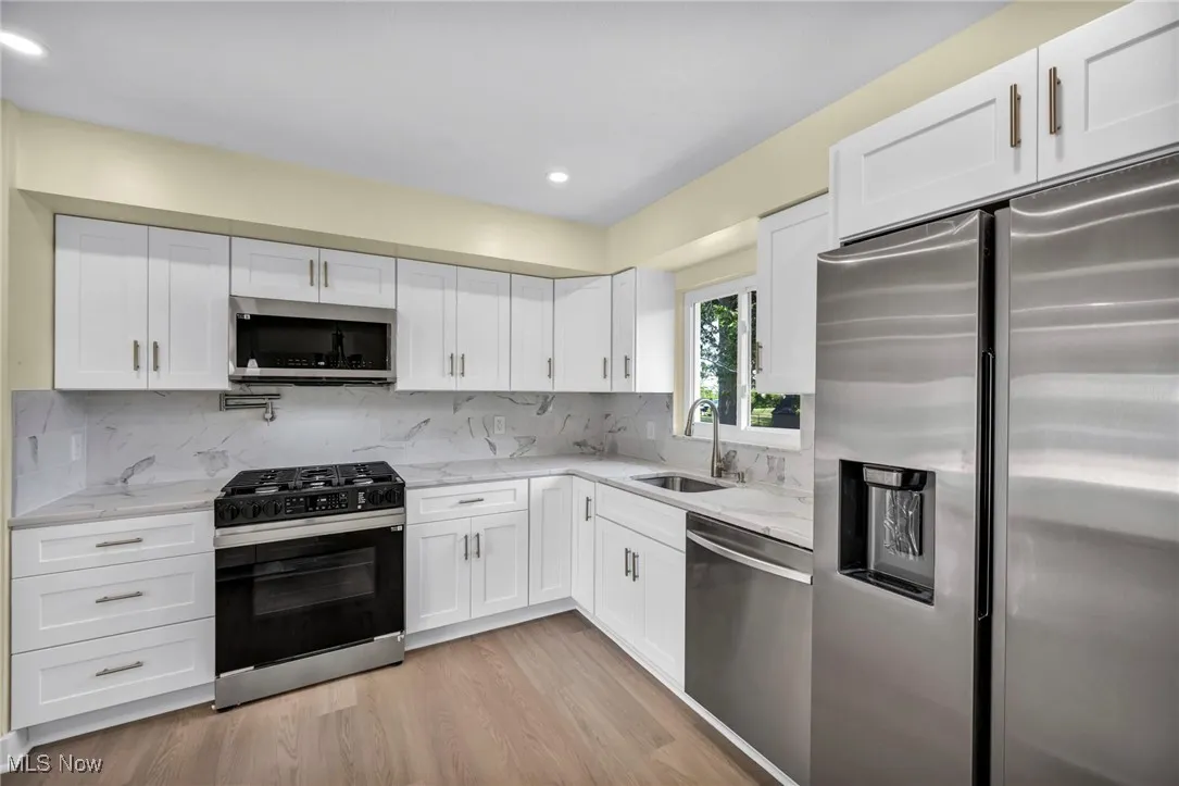 Kitchen featuring appliances with stainless steel finishes, tasteful backsplash, white cabinetry, light wood-style flooring, and light stone countertops
