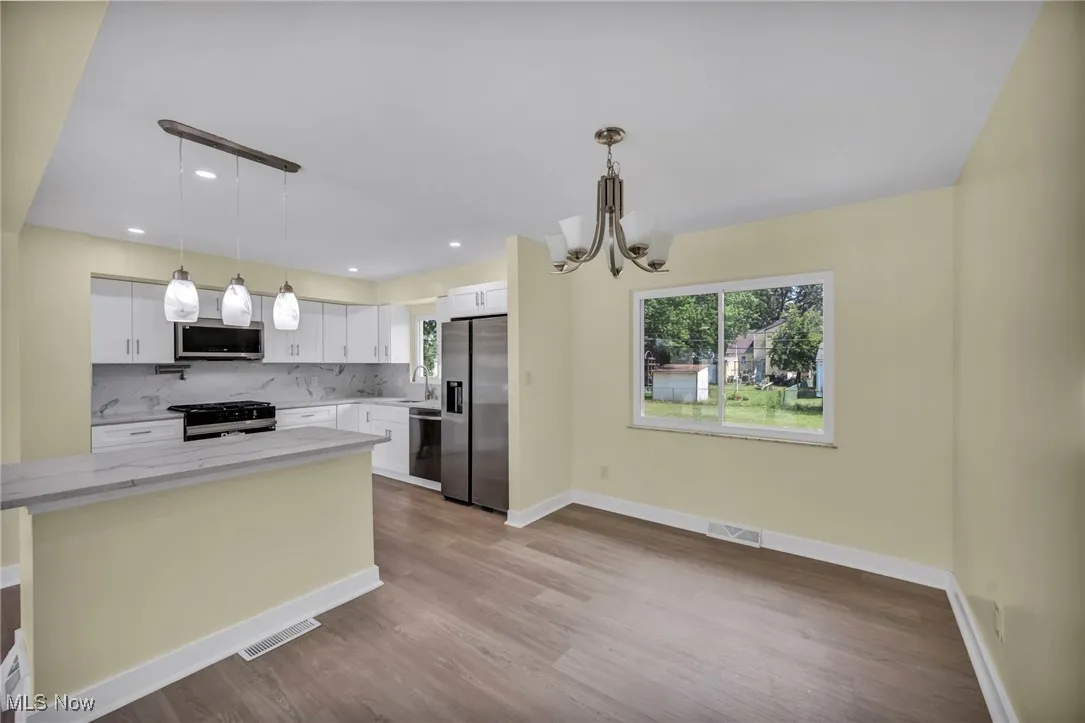 Kitchen with stainless steel appliances, a chandelier, wood finished floors, light stone counters, and white cabinetry
