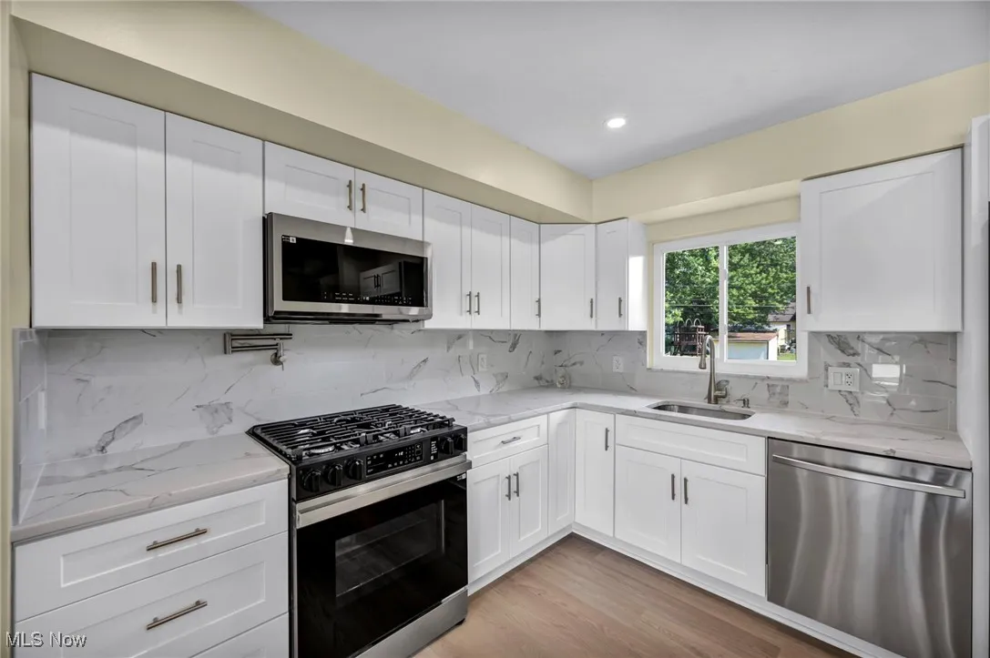 Kitchen featuring stainless steel appliances, tasteful backsplash, light wood-type flooring, white cabinetry, and light stone countertops