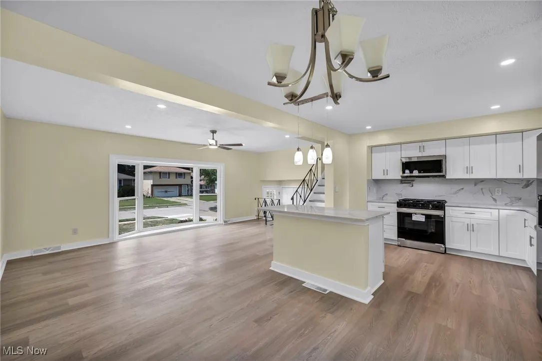 Kitchen with decorative backsplash, open floor plan, stainless steel appliances, a kitchen island, and a chandelier
