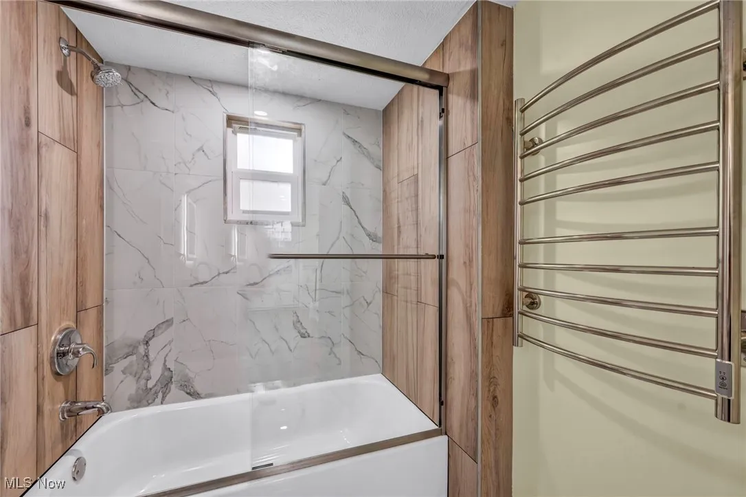 Bathroom featuring radiator heating unit, shower / washtub combination, and a textured ceiling