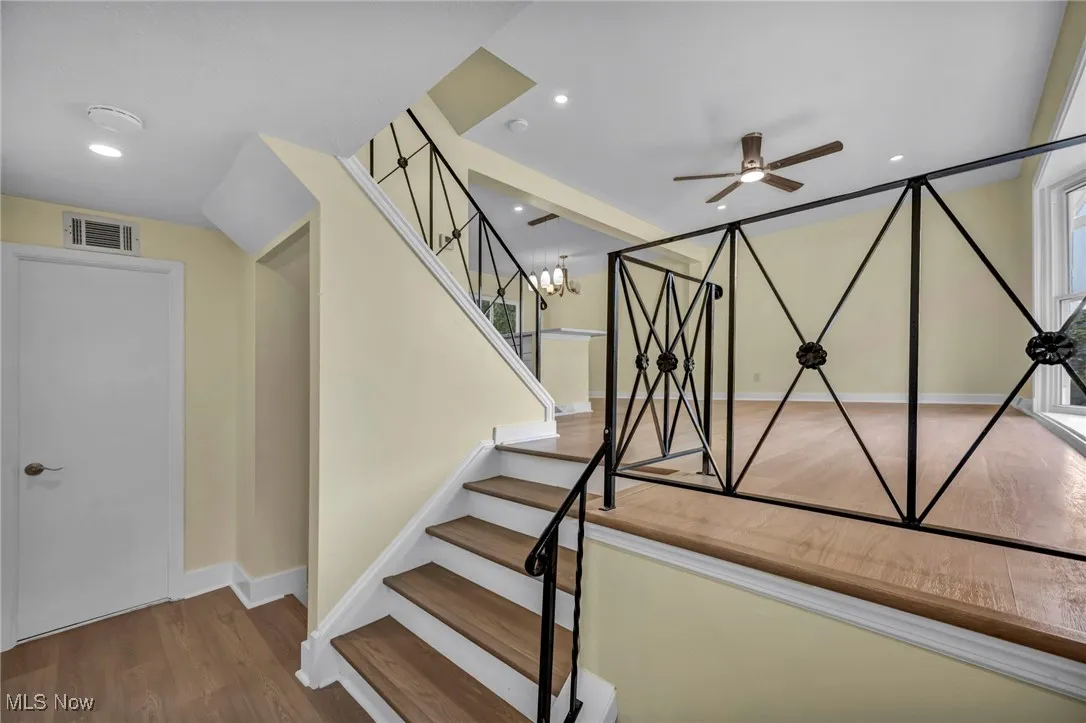 Stairs featuring wood finished floors, a chandelier, ceiling fan, and recessed lighting